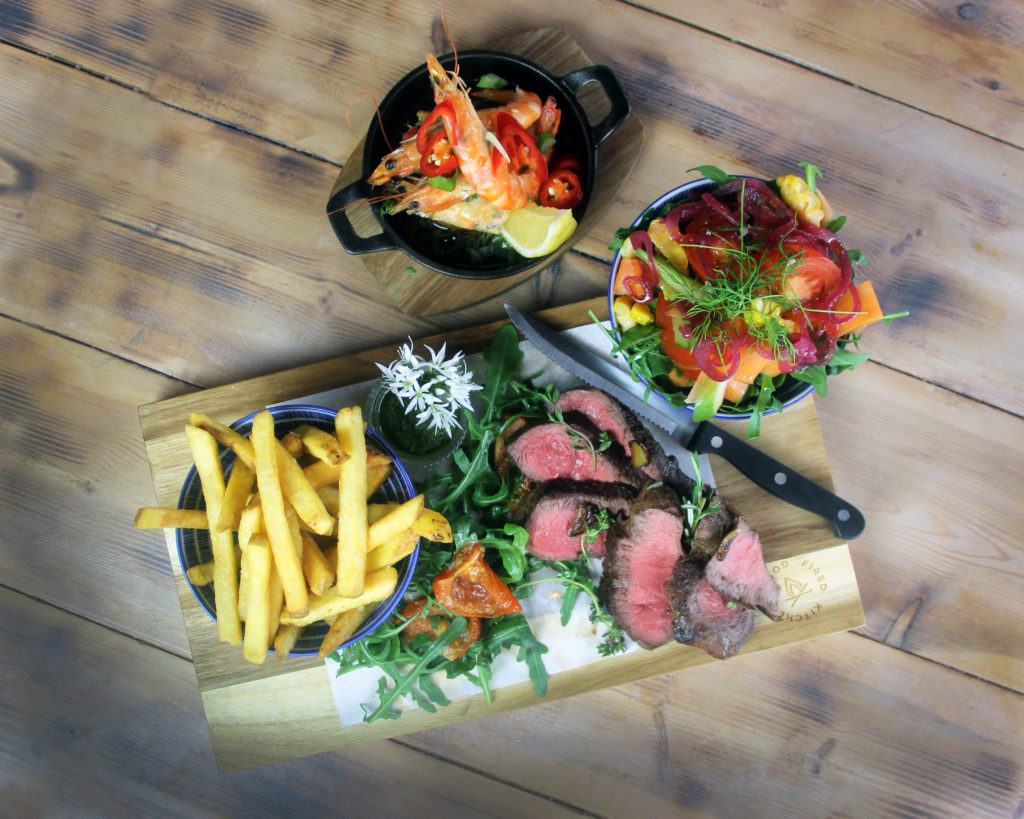 Sliced steak, pink in the middle, with chips, rocket and roasted tomato on a wooden board